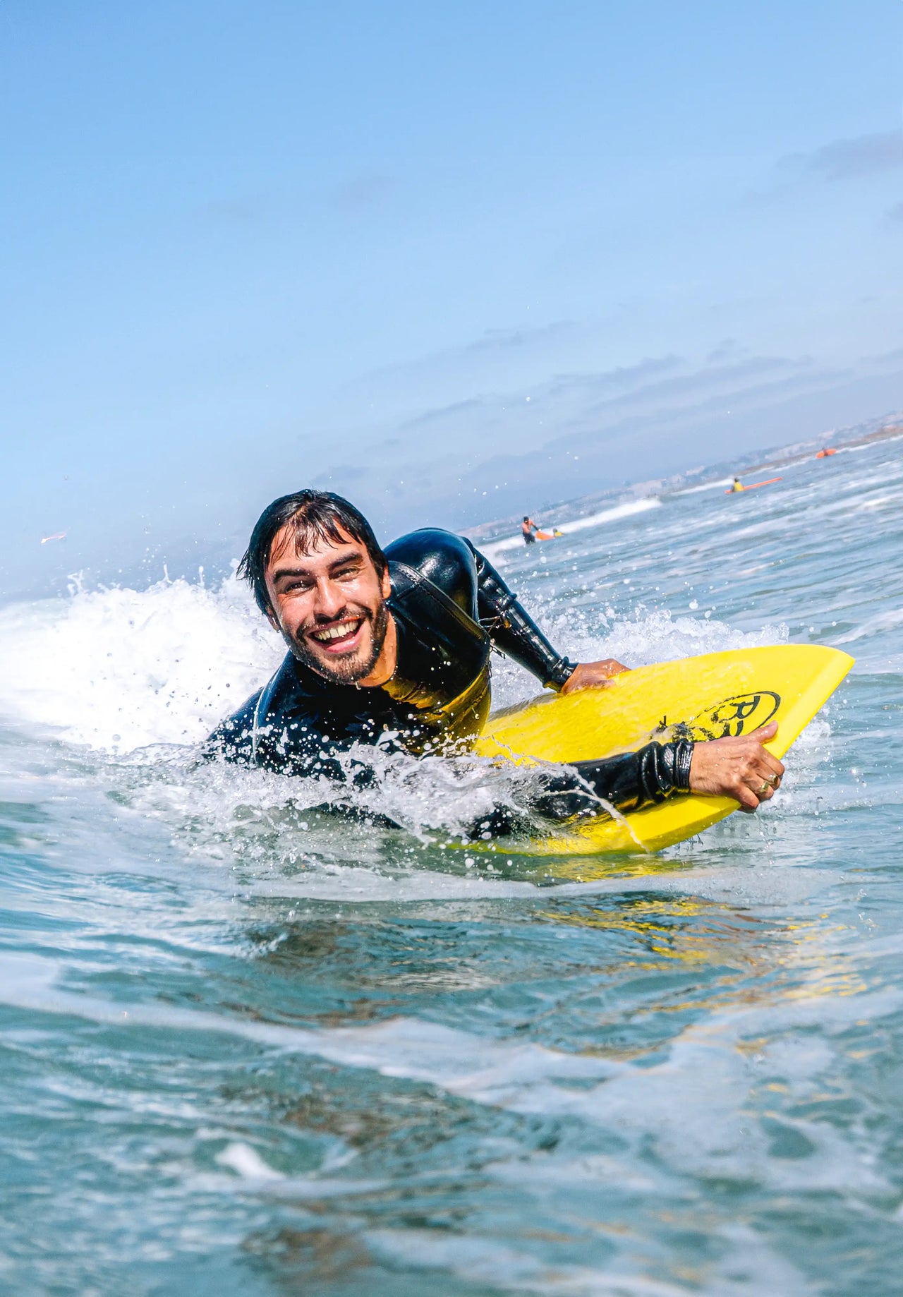 Smiling surfer riding a wave on a yellow BZ Pro Boards bodyboard in the ocean