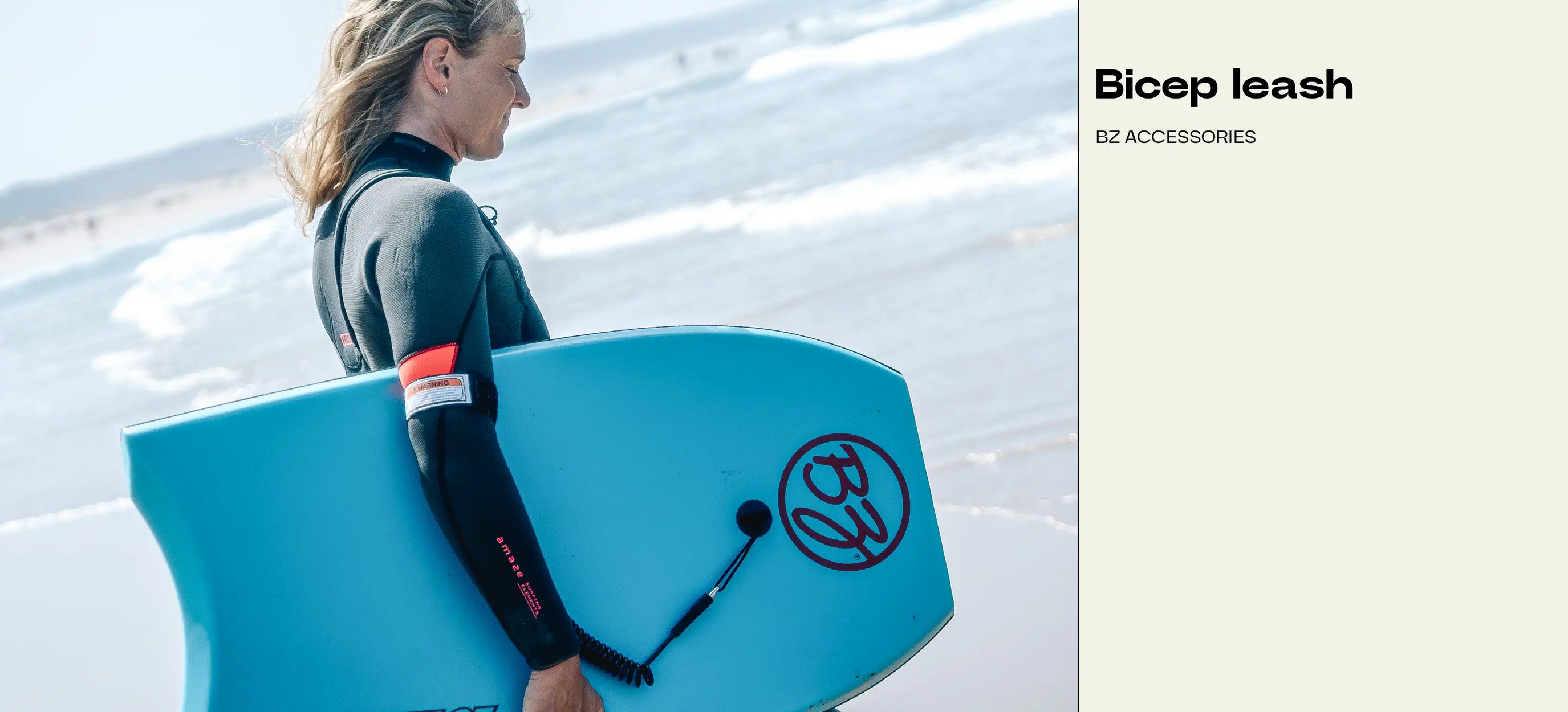 Woman in wetsuit holding blue BZ Pro Board with bicep leash at beach
