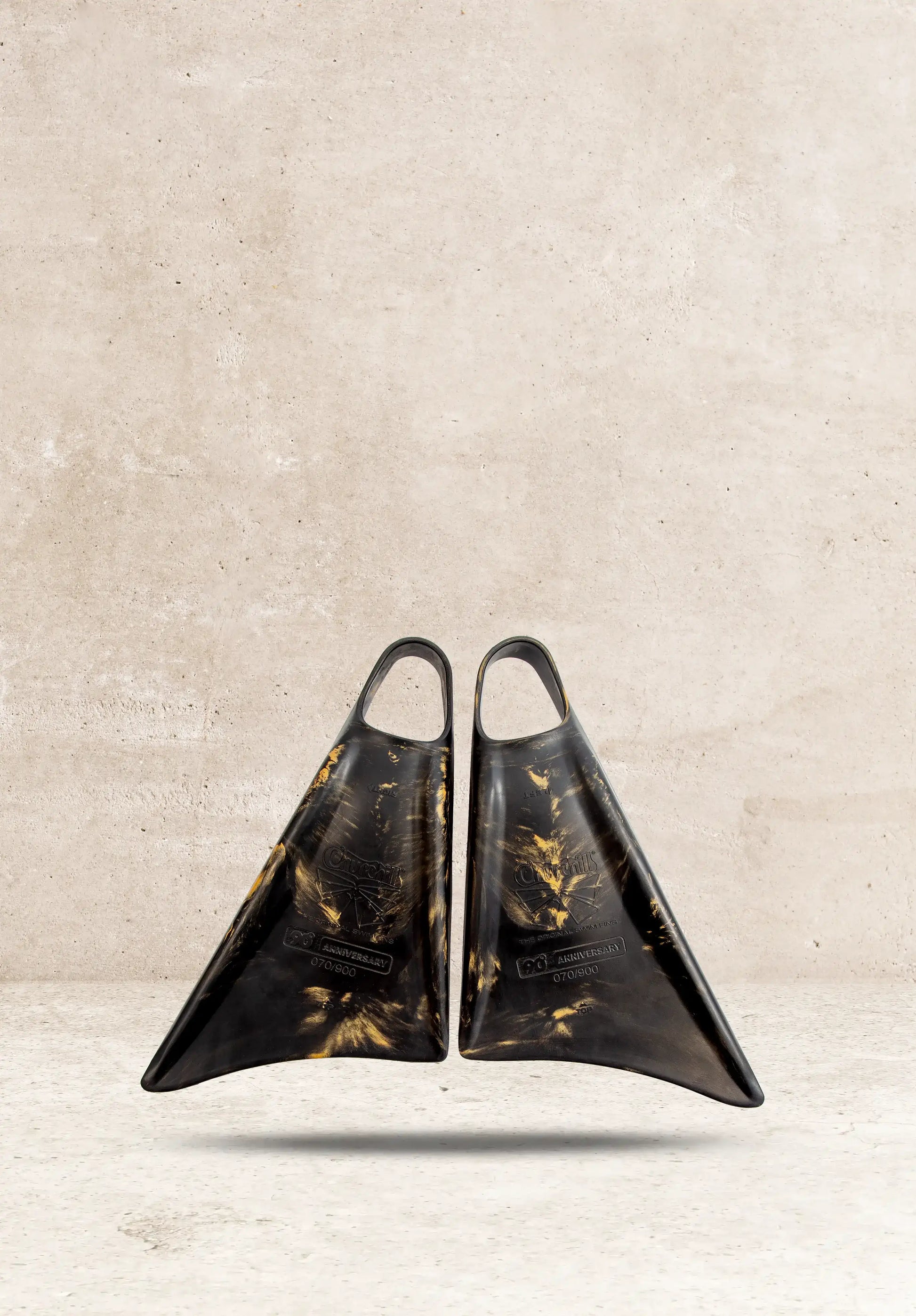 Churchill 90th Anniversary swim fins, black with gold accents, displayed against concrete background