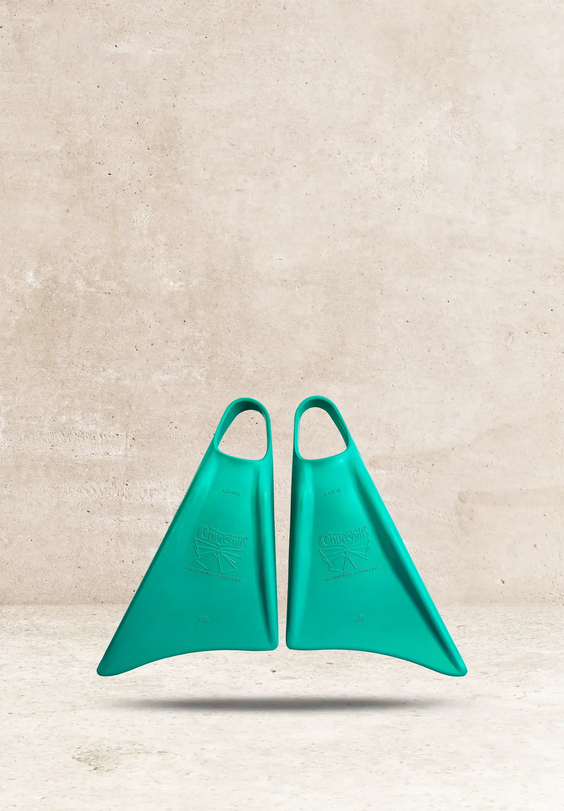 Teal Churchill swim fins, original design, against concrete background