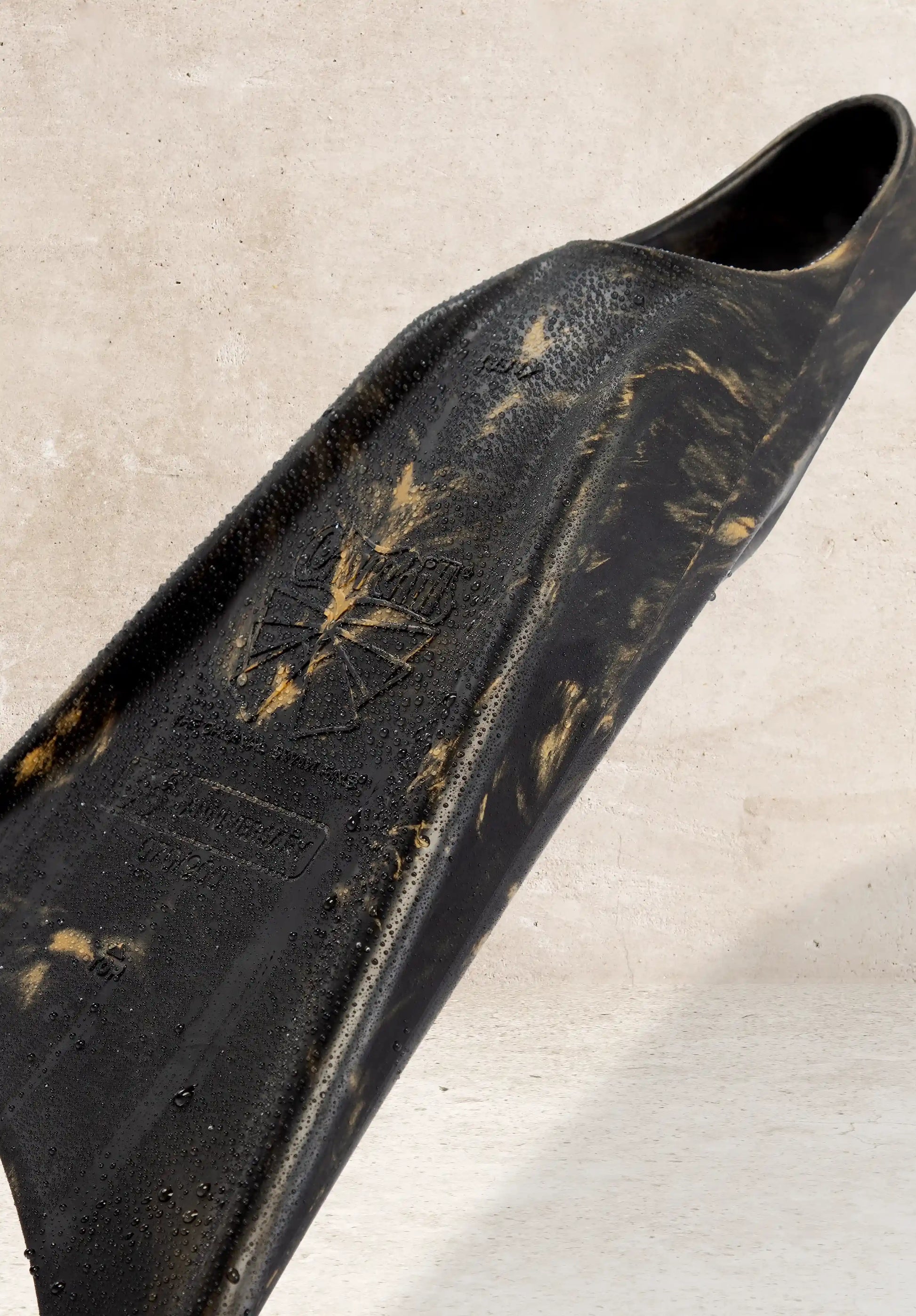Wet black bodyboard with gold accents and textured grip, resting on concrete surface.