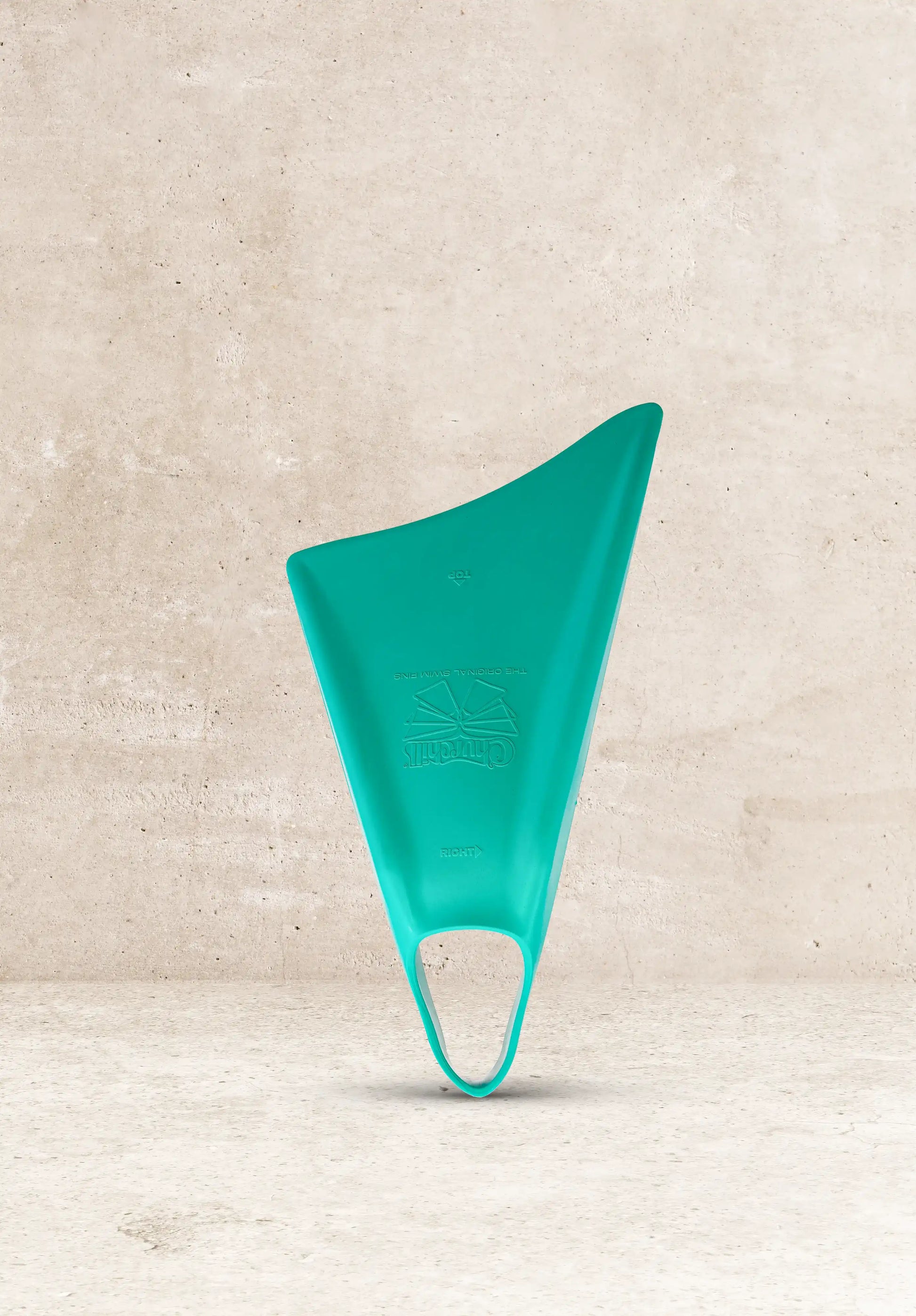 Teal Churchill swim fin for bodyboarding, standing against concrete background