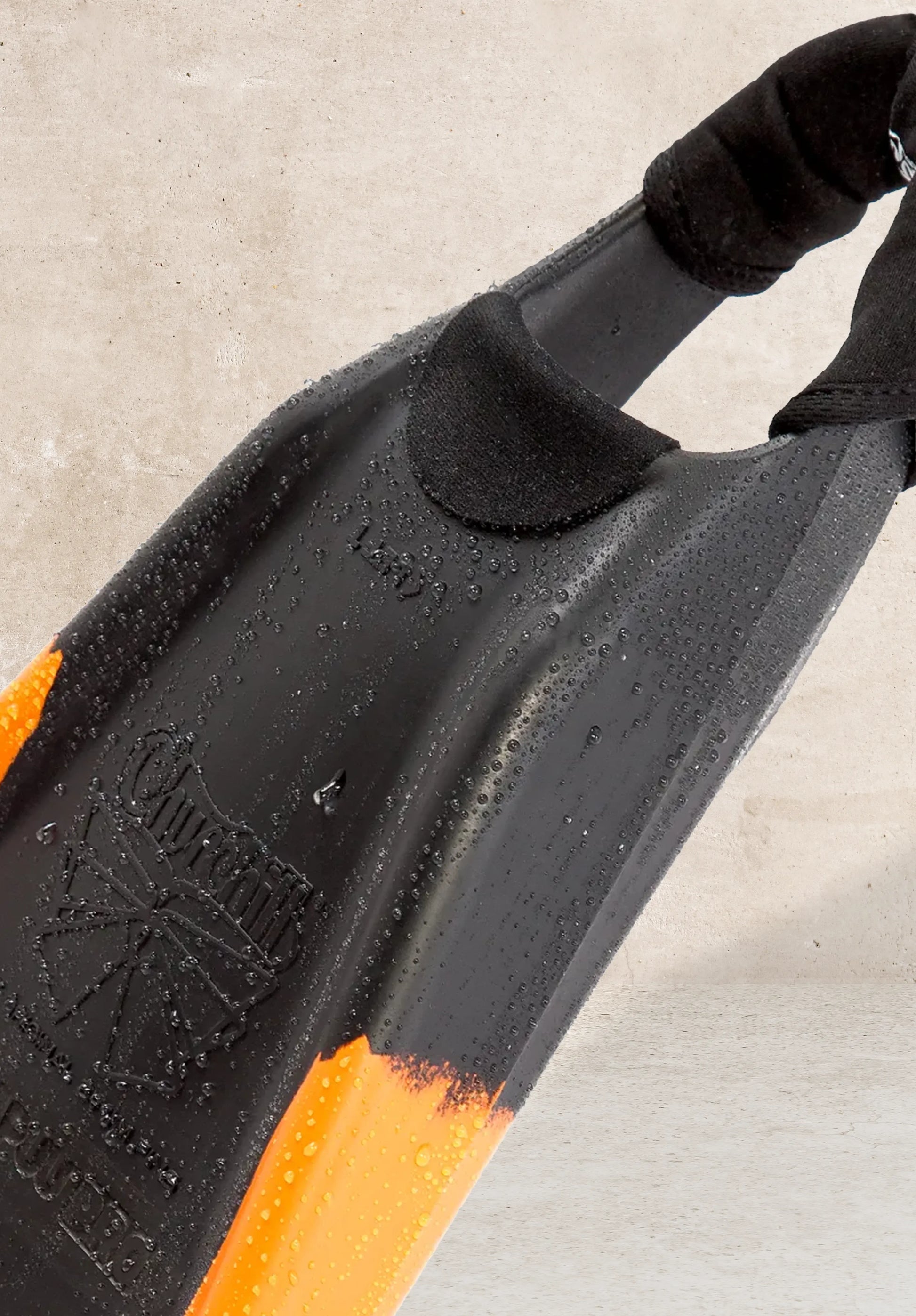 Black and orange boogie board with textured grip and water droplets on concrete surface