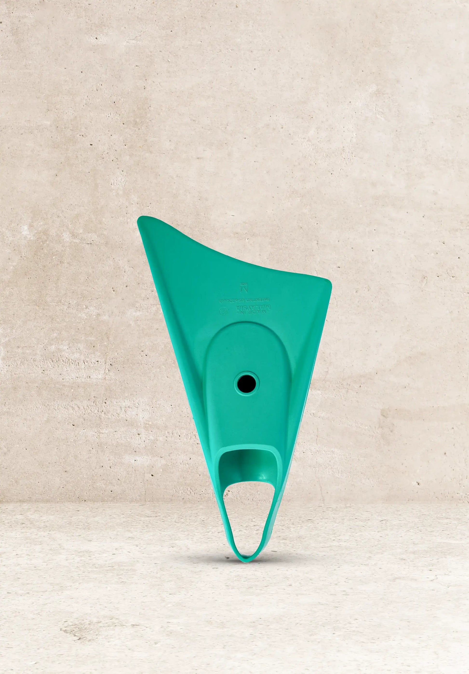 Teal boogie board tail fin for wave riding, size M, against concrete background